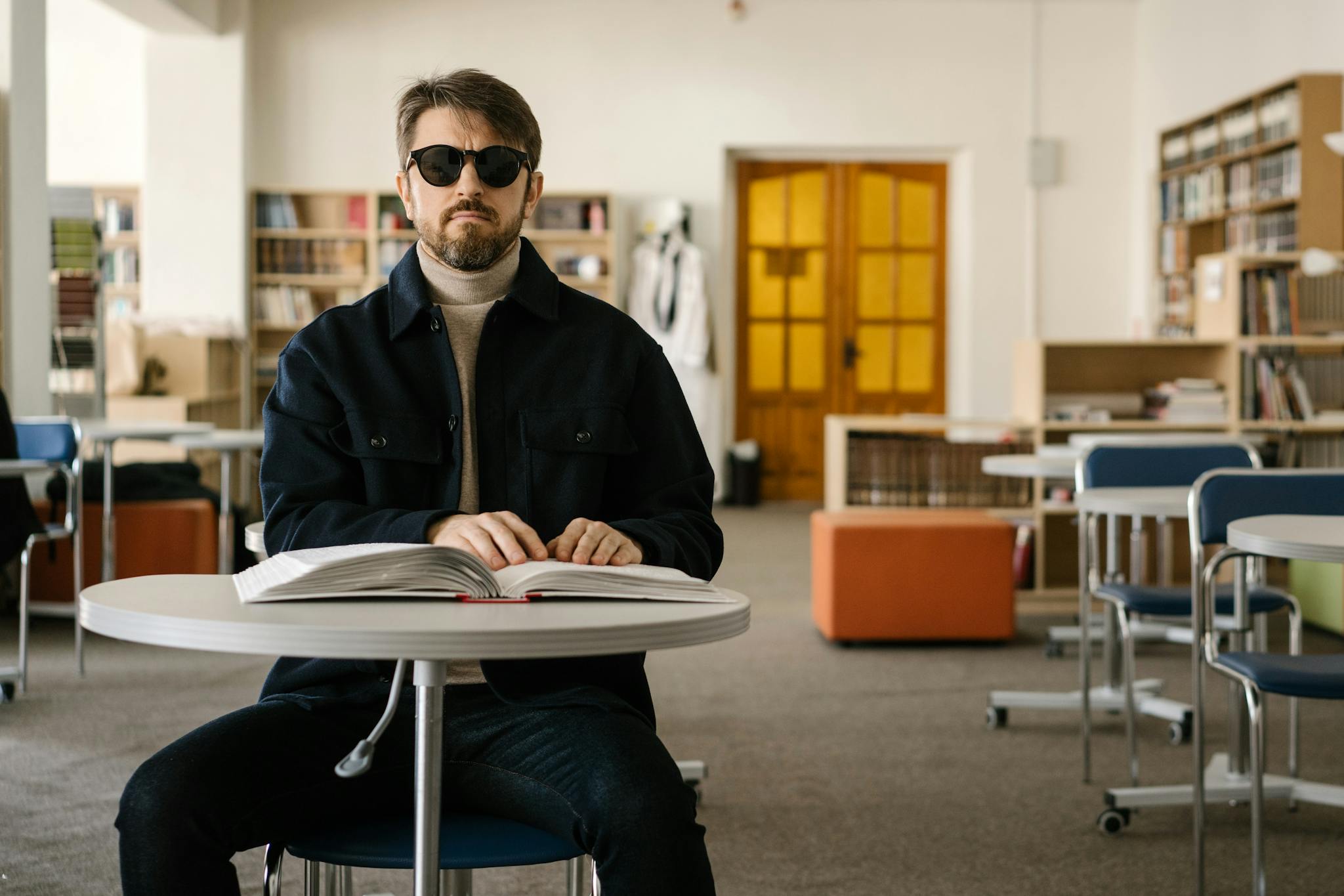 About Visually impaired man reads Braille book in an indoor library setting.